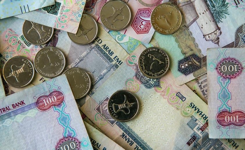 Notas de papel Dubai espalhadas sobre uma mesa com moedas de 1 dirham acima.