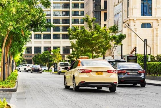 Carros em Dubai na estrada, um táxi em primeiro plano, casas ao fundo.