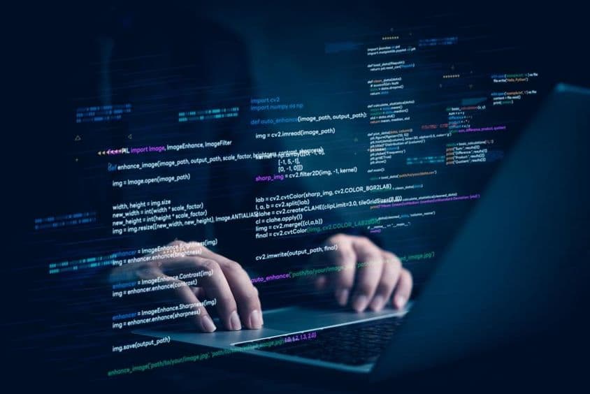 Um notebook com duas mãos trabalhando, projetando um trecho de código de computador.