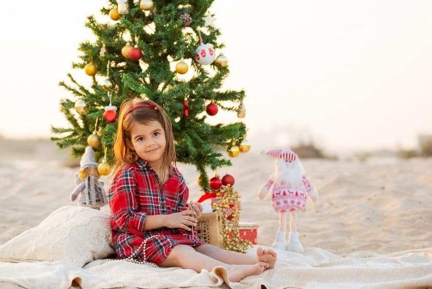 Menina feliz sorrindo na praia embaixo de uma árvore de Natal.