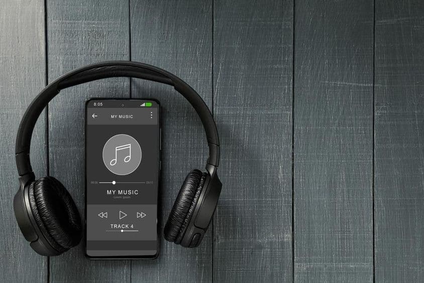 Reprodução de música circulando em um telefone, com fones de ouvido ao lado.