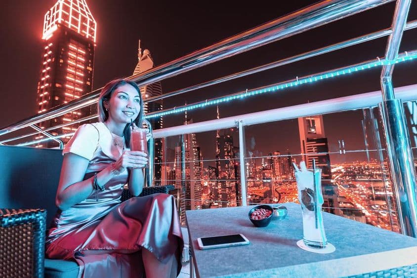 Jovem mulher bebendo coquetel no terraço de um bar rooftop em Dubai.