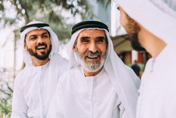 Um idoso Emirati conversando com dois indivíduos mais jovens.