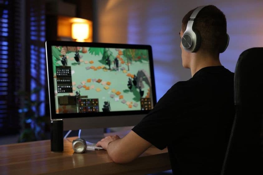 Uma criança mais velha joga um videogame em um computador em uma mesa.