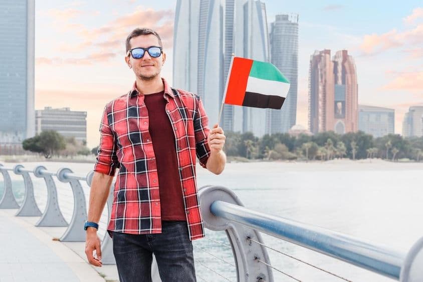 Homem jovem na Marina de Dubai segurando uma bandeira dos Emirados Árabes Unidos.