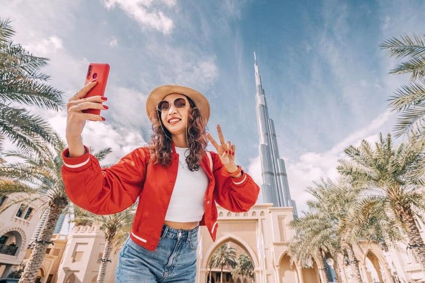 Jovem mulher, de blusa vermelha, tirando uma selfie com o Burj Khalifa ao fundo.