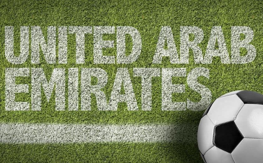 Inscrição de EAU pintada na grama com uma bola de futebol.