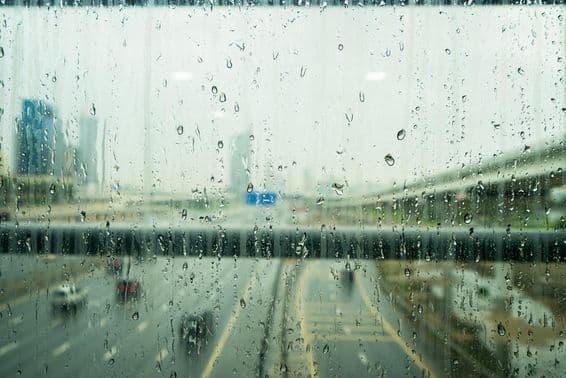 Gotas de chuva em uma janela com alguns arranha-céus desfocados ao fundo.