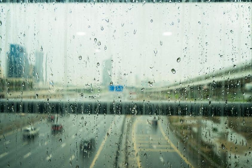 Gotas de chuva em uma janela com alguns arranha-céus desfocados ao fundo.