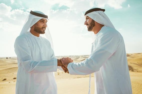 Dois homens árabes apertando as mãos no deserto.