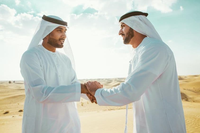 Dois homens árabes apertando as mãos no deserto.