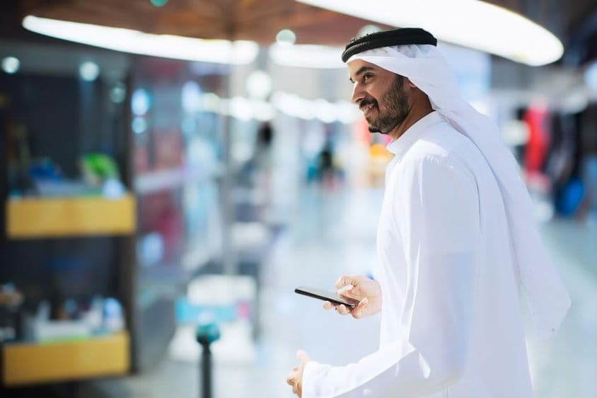 Homem árabe no aeroporto de Dubai segurando um telefone.