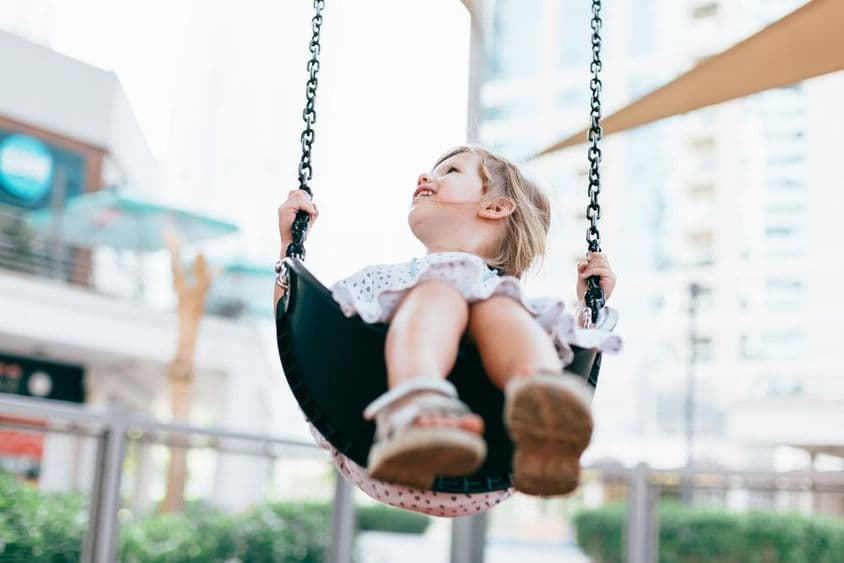 Garotinha feliz balançando no pátio do jardim de infância.