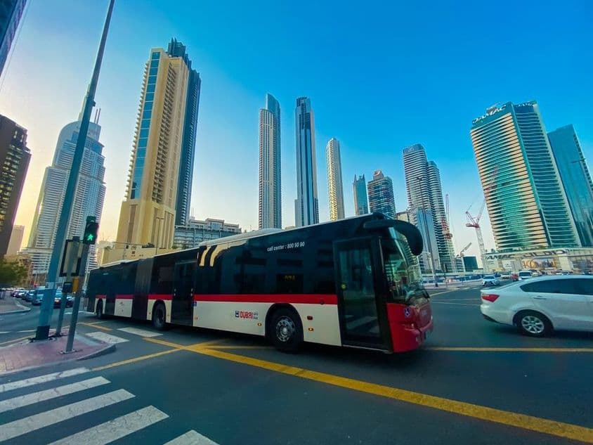 Ônibus de Dubai com arranha-céus ao fundo.