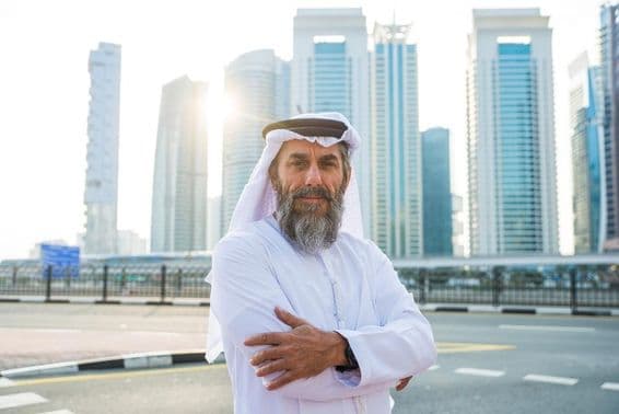 Homem idoso em Dubai com arranha-céus ao fundo.