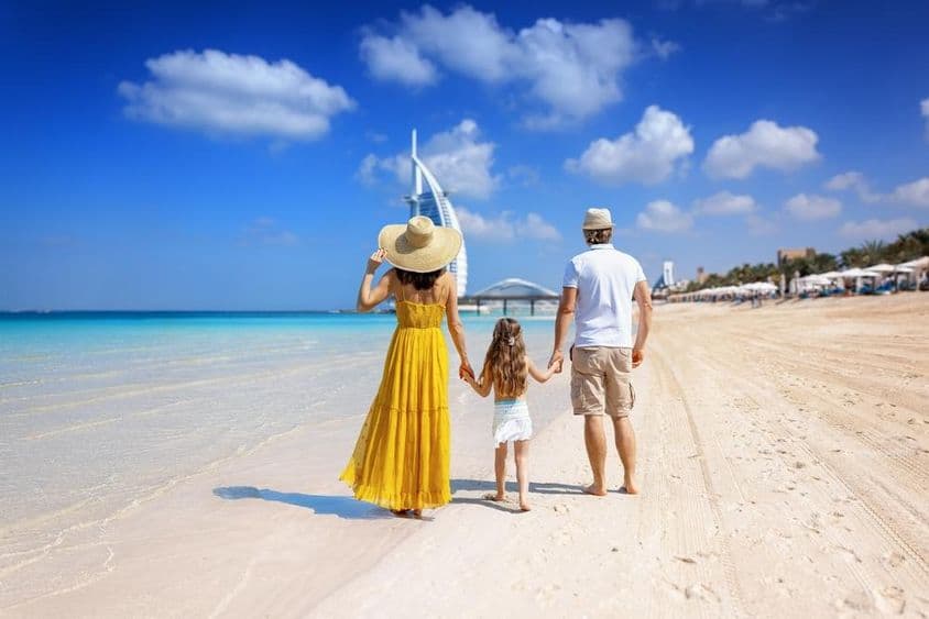 Uma família caminhando em uma praia de Dubai com o Burj al Arab ao fundo.