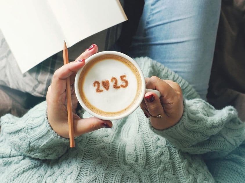 Uma xícara de café segurada por uma mão feminina, com 2025 escrito dentro.