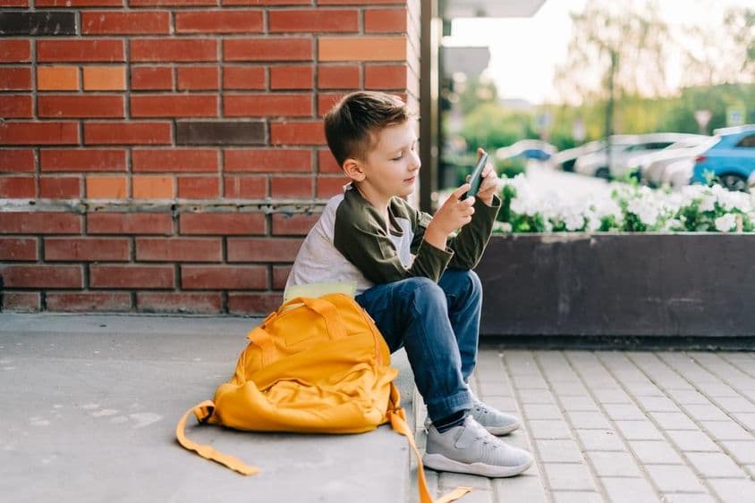 Garoto usando um telefone nos degraus da escola.
