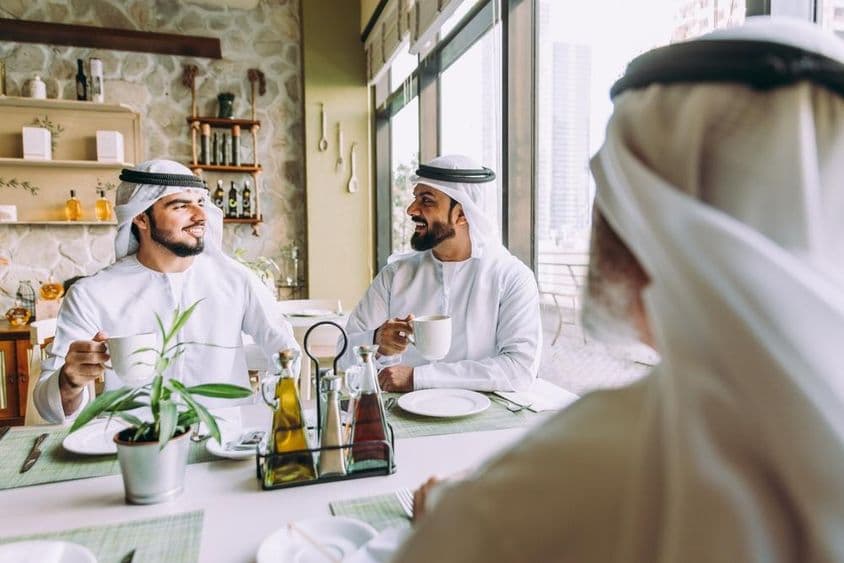 Três empresários tomando chá em Dubai, vestindo trajes tradicionais emiradenses.