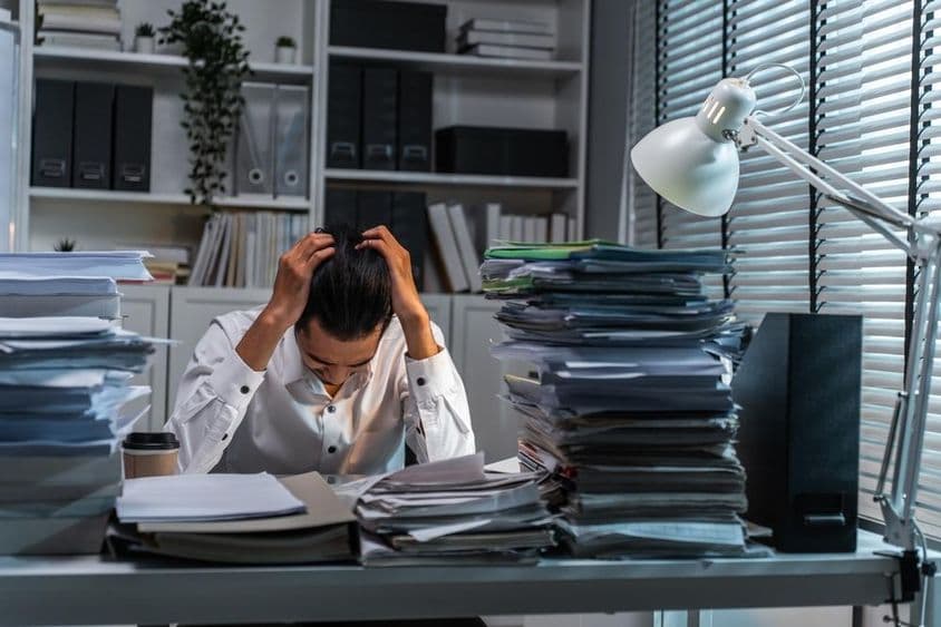Trabalhador de escritório segurando a cabeça devido a sobrecarga de trabalho.