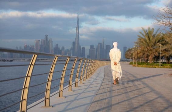 Homem Emiradense caminhando em uma calçada com o Burj Khalifa ao fundo.