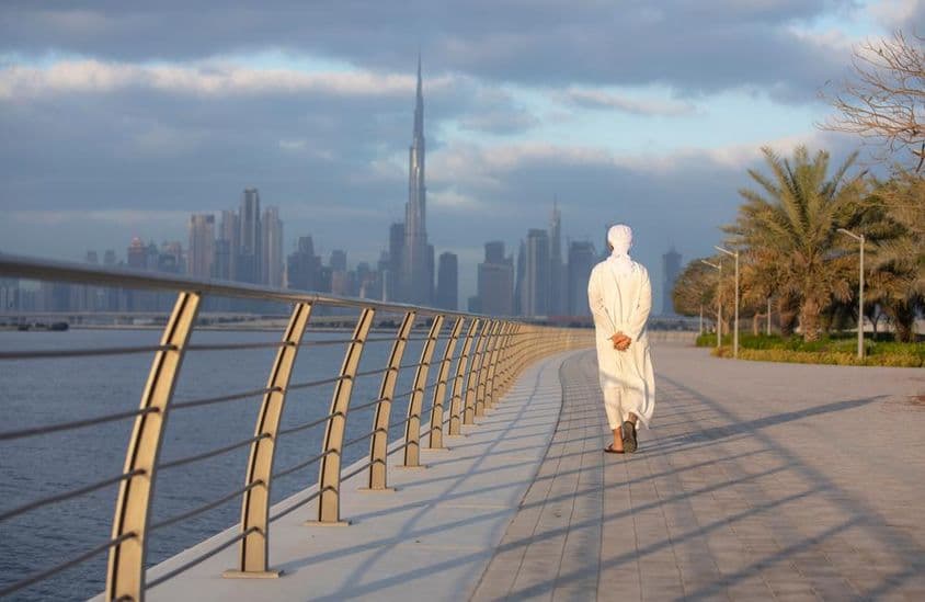 Homem Emiradense caminhando em uma calçada com o Burj Khalifa ao fundo.