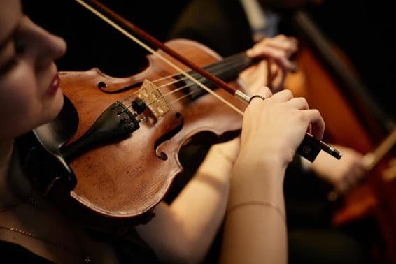 Música de orquestra feminina tocando violino com arco durante um concerto no palco.