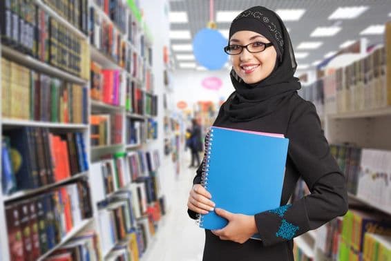 Estudante árabe na biblioteca com caderno na mão.