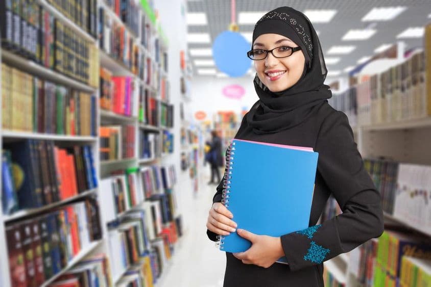 Estudante árabe na biblioteca com caderno na mão.