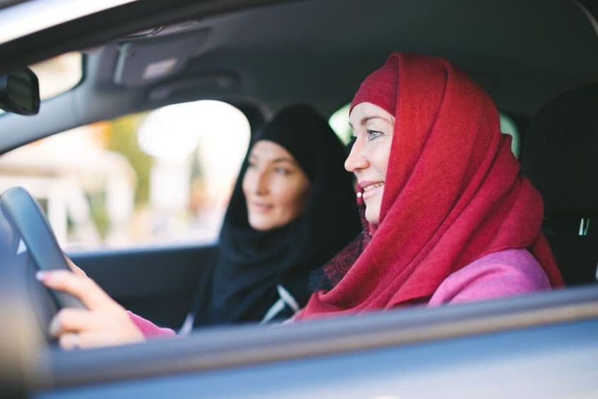 Mulher muçulmana dirigindo um carro, transportando outra mulher muçulmana.