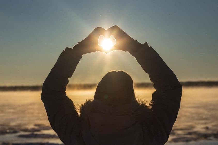 Mulher formando corações com as mãos ao ar livre em um pôr do sol gelado.