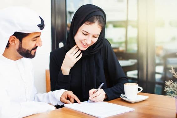 Homem árabe entregando documentos para assinatura a uma mulher usando hijab.