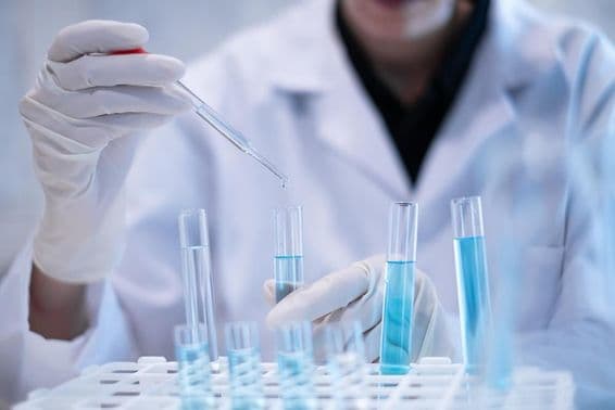 Cientista pipetando líquido azul em um tubo de ensaio em um laboratório.