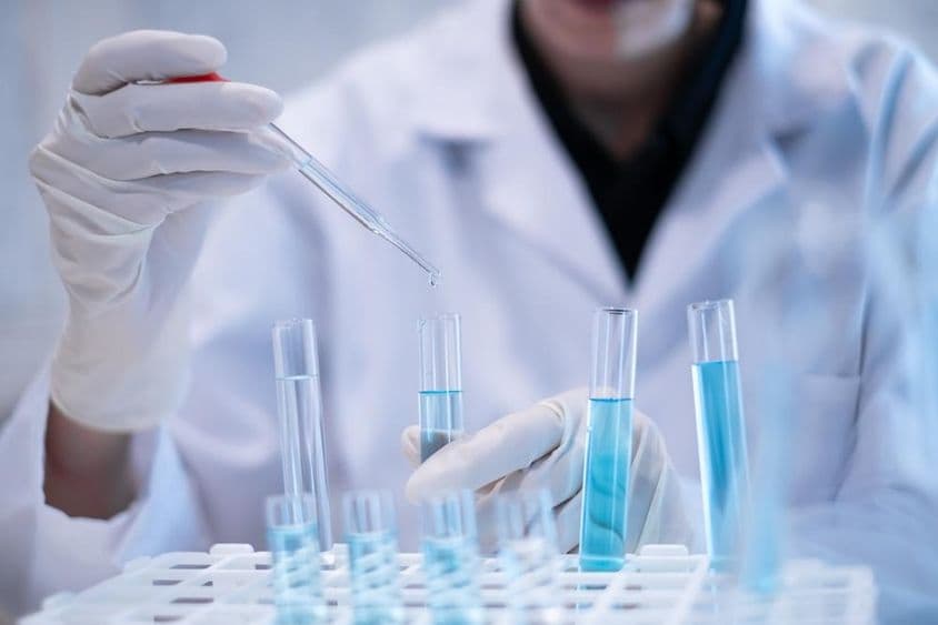 Cientista pipetando líquido azul em um tubo de ensaio em um laboratório.