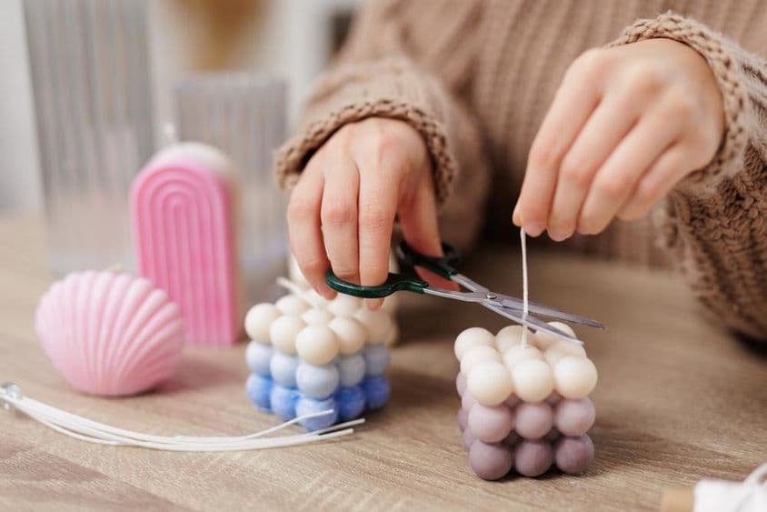 Vela decorativa em uma mesa, menina corta o pavio.