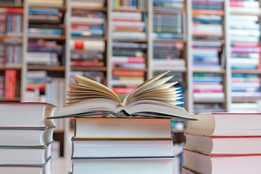 Romance aberto sobre uma pilha de livros em frente a uma estante.