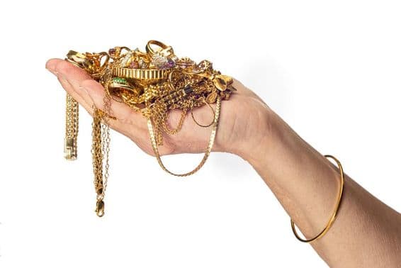 A mão de uma mulher segurando uma pilha de joias de ouro e usando uma pulseira.