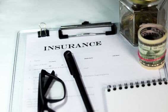 Formulário de seguro com caixa de moedas, maço de dólares, caneta e óculos.