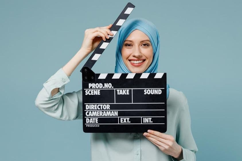 Jovem mulher árabe muçulmana em abaya hijab segurando uma claquete clássica de filme preta.