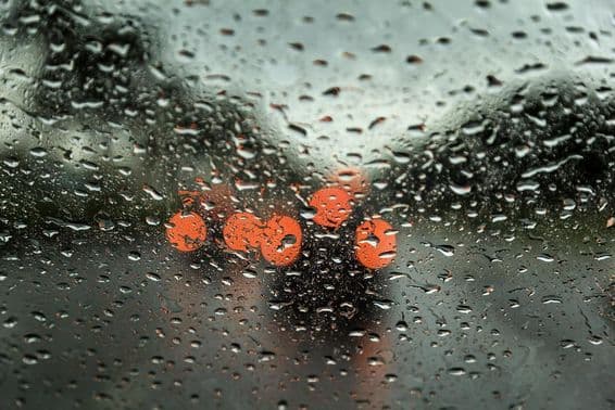 Dia chuvoso em Dubai com luzes de carros visíveis à distância, visualizado através de uma janela de carro com gotas de chuva.