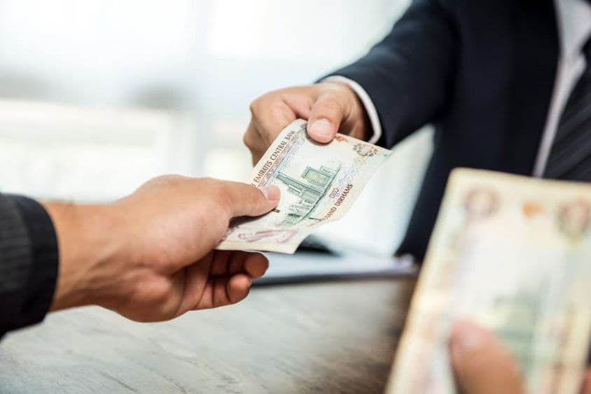 Empresário entregando dinheiro em moeda dirham dos Emirados Árabes Unidos a um parceiro.