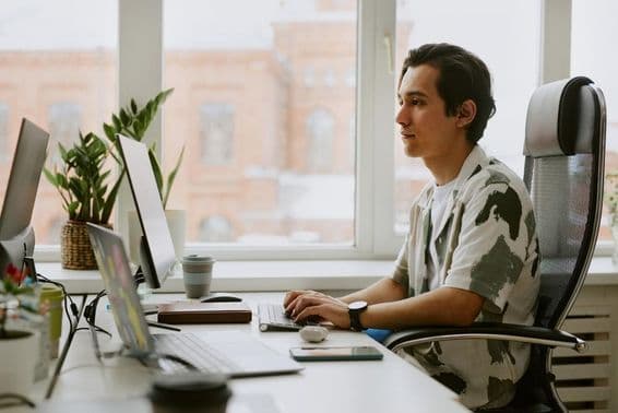 Jovem programador sentado à mesa, codificando em um computador em um escritório iluminado.