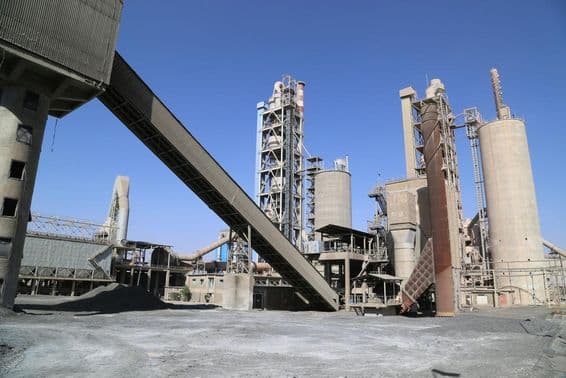 Fábrica de cimento com torres e esteira transportadora.