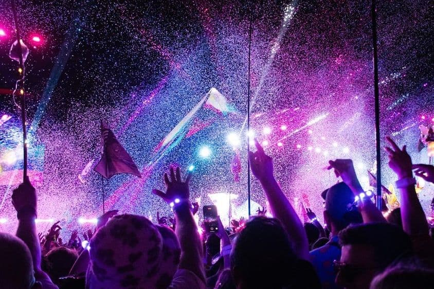 Festival de música, palco, multidão animada com mãos levantadas.
