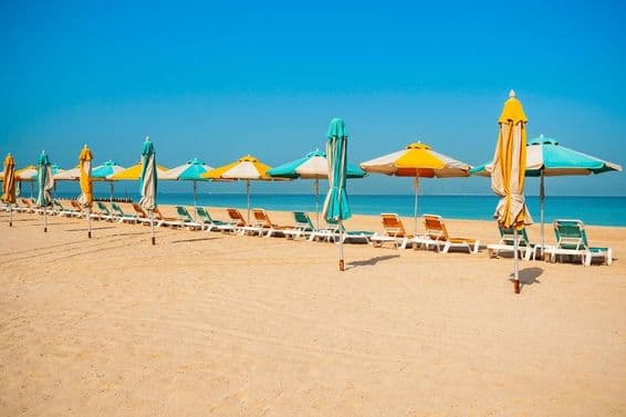 Praia pública de Dubai, areia, espreguiçadeiras e mar azul.