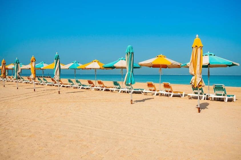 Praia pública de Dubai, areia, espreguiçadeiras e mar azul.