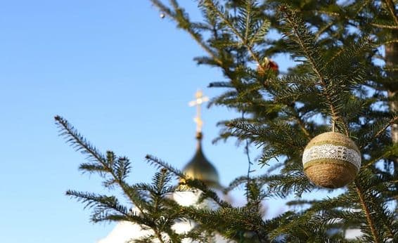 Galho de árvore de Natal com enfeites e uma cruz ortodoxa ao fundo