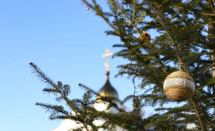 Galho de árvore de Natal com enfeites e uma cruz ortodoxa ao fundo