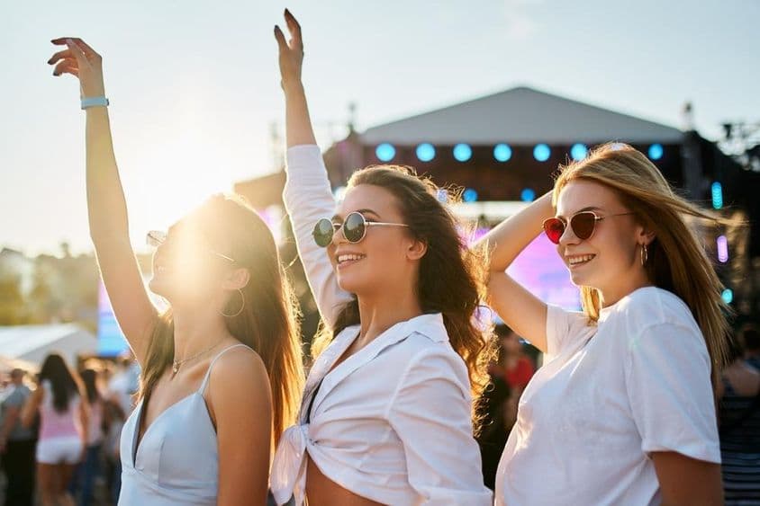 Garotas em vestidos de verão curtindo um show, celebrando com as mãos levantadas.
