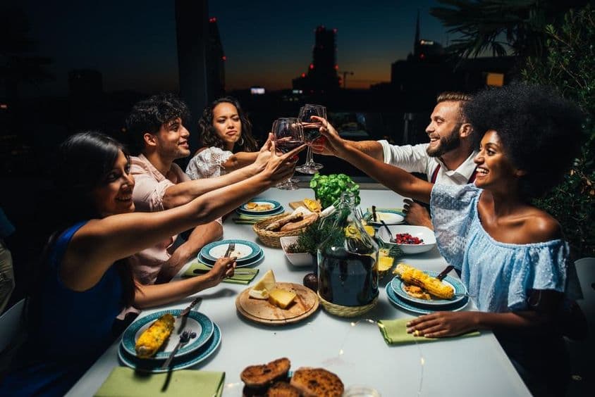 Grupo de amigos desfrutando de uma refeição e comemorando em uma bela varanda de cobertura.